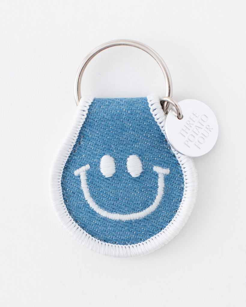 denim rounded keychain with white embroidered smiley face