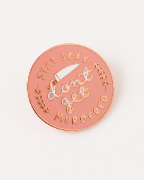 funny pink pin with white text 'stay sexy don't get murdered' gold accents and knife illustration