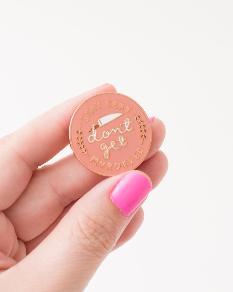 funny pink pin with white text 'stay sexy don't get murdered' gold accents and knife illustration